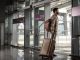 Bărbat cu rucsac și troler care iese din terminalul unui aeroport pentru a prelua o mașină închiriată.